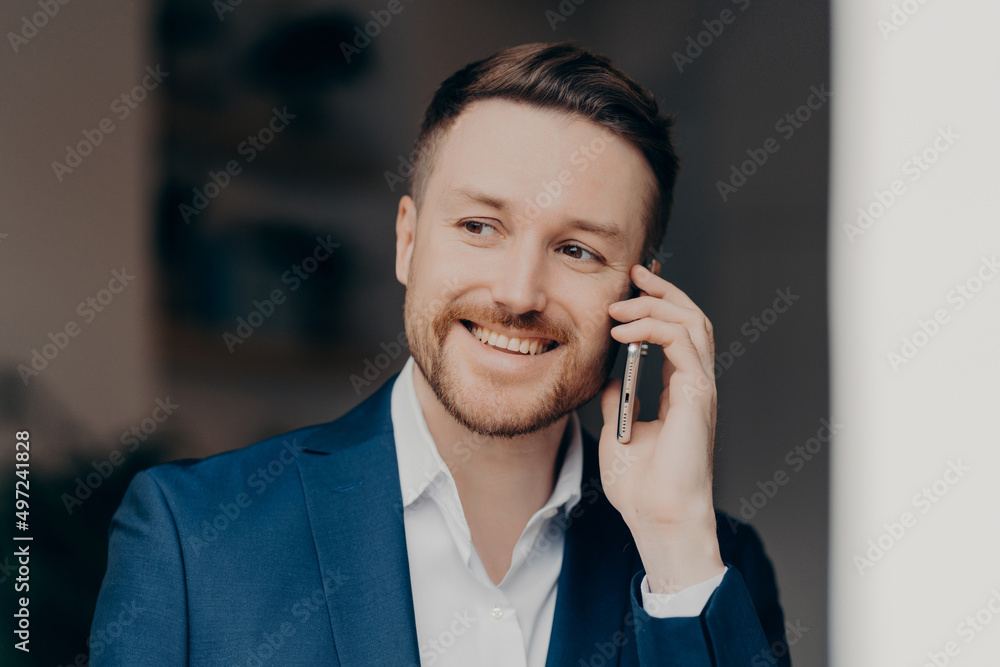 Smiling young man in suit using mobile phone at home Smiling young man in suit using mobile phone at home