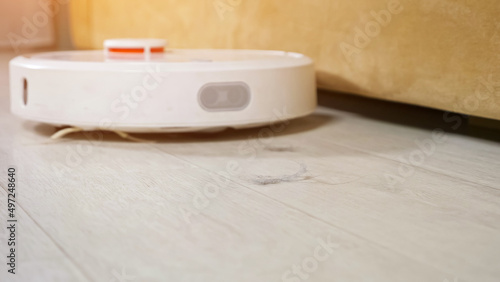 The robot vacuum cleaner cleans the floor in the room. Technologies that help housewives clean the apartment, sunlight