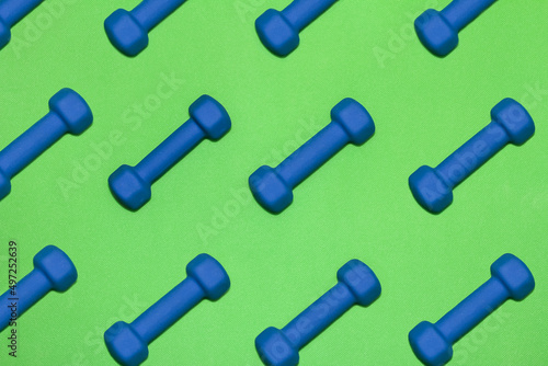 Rows of blue dumbbells on bright green gym mat 