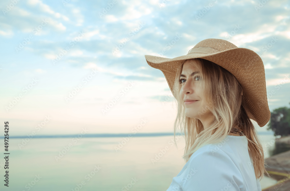 Portrait of young 30 year european woman in a straw hat and white dress looking side on a sea beach background. Nude make-up. Beautiful girl. Side view. Profile. Dreamed mood. International woman day