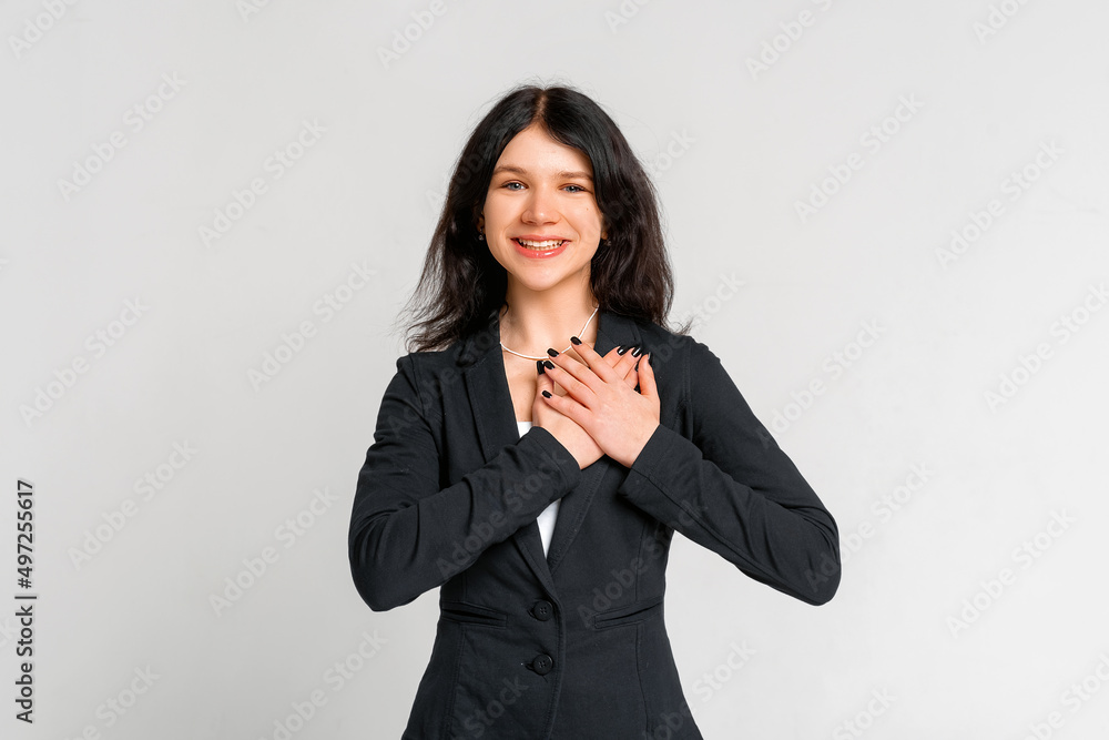 Smiling beautiful brunette teen girl laughing, holding hand on heart appreciation gesture, grateful, say thank you, being pleased, receive compliment, gray background Smiling beautiful brunette teen girl laughing, holding hand on heart appreciation gesture, grateful, say thank you, being pleased, receive compliment, gray background