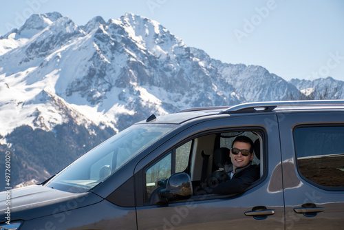Man looking out from car with snowy mountains background in Loudenvielle, France