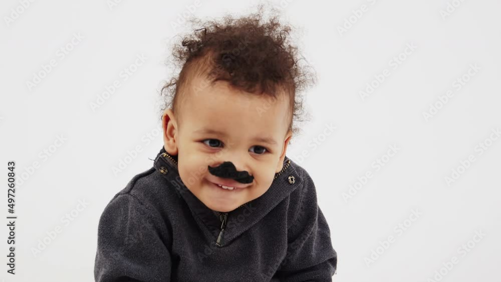 little African American curly boy with big black eyes putting on fake toy mustache looking into the camera studio shot. High quality 4k footage little African American curly boy with big black eyes putting on fake toy mustache looking into the camera studio shot. High quality 4k footage