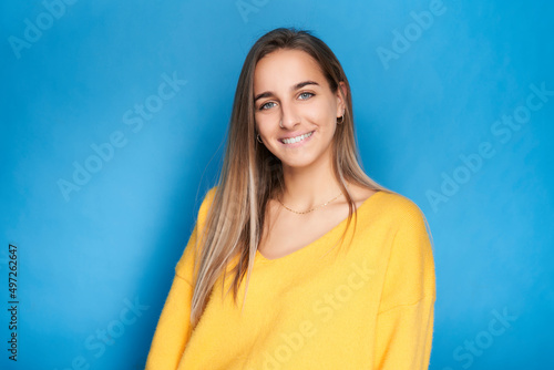 Portrait of young girl looking at camera smiling with yellow sweater and blue background