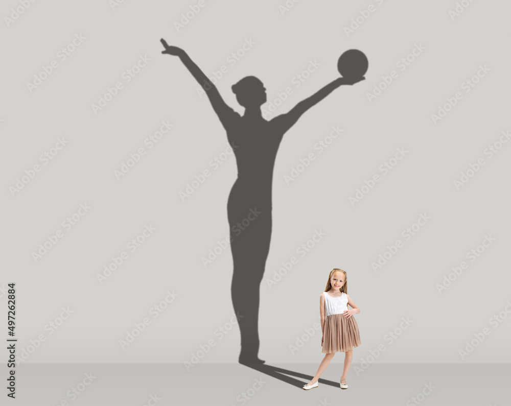 Kids and future. Conceptual image with little girl dreaming about becoming gymnast isolated on studio gray wall. Focus on shadow
