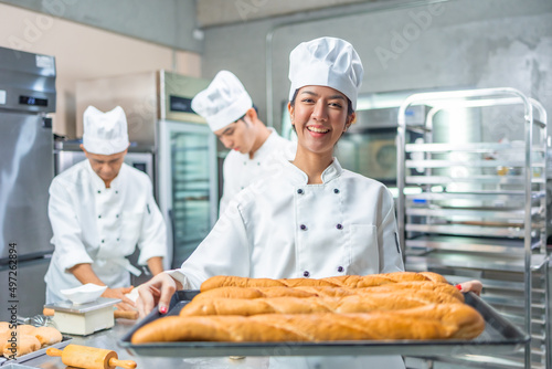 Smiling asian young female bakers looking at camera..Chefs baker in a chef dress and hat, cooking together in kitchen.Team of professional cooks in uniform preparing meals in the kitchen.