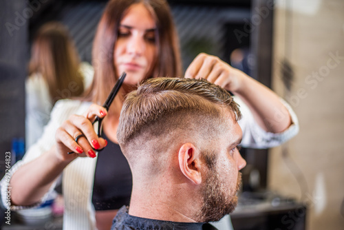 Barber cutting with scissors bearded man in barbershop