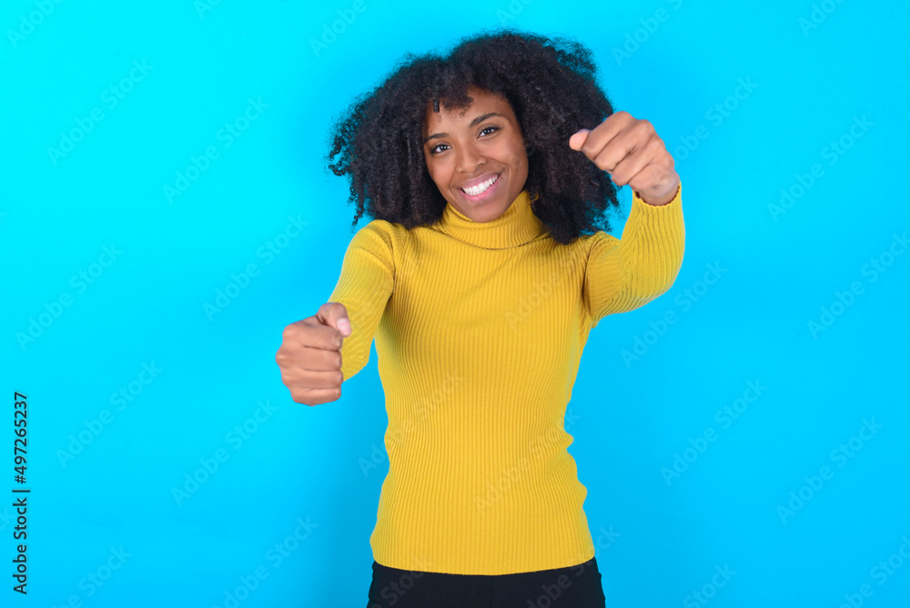 Young woman with afro hairstyle wearing yellow turtleneck over blue background imagine steering wheel helm rudder passing driving exam good mood fast speed Young woman with afro hairstyle wearing yellow turtleneck over blue background imagine steering wheel helm rudder passing driving exam good mood fast speed