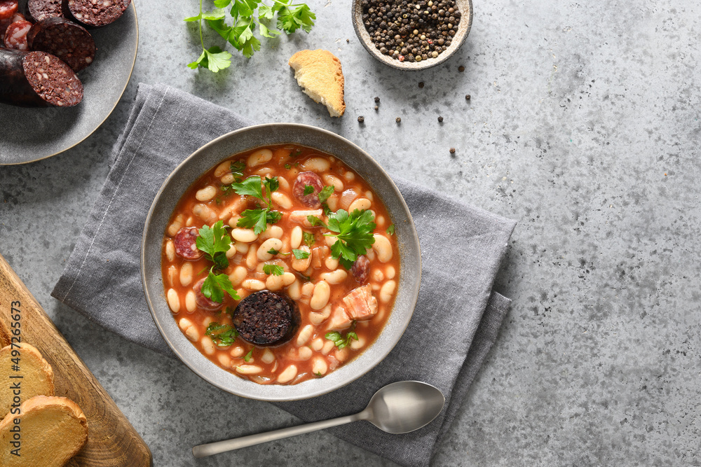 Spanish fabada served on gray stone background. Fabada makes of haricot, chorizo, morcillas or blood sausage, tomatoes. View from above. Copy space. Spanish fabada served on gray stone background. Fabada makes of haricot, chorizo, morcillas or blood sausage, tomatoes. View from above. Copy space.