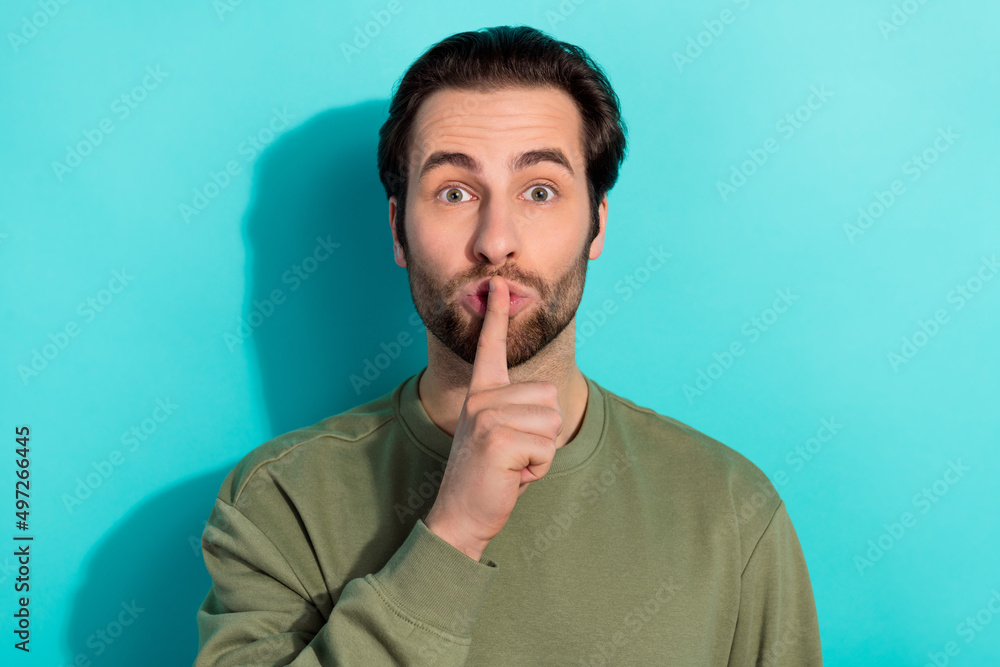 Photo of silent beard young guy finger mouth wear khaki sweatshirt isolated on teal color background Photo of silent beard young guy finger mouth wear khaki sweatshirt isolated on teal color background