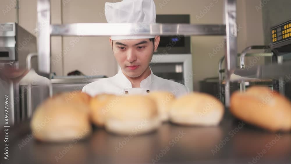 Smiling bakers looking at camera..Chef baker in a chef dress and hat, cooking together in kitchen.Young asian man takes fresh baked cookies out of modern electric oven in kitchen. Smiling bakers looking at camera..Chef baker in a chef dress and hat, cooking together in kitchen.Young asian man takes fresh baked cookies out of modern electric oven in kitchen.