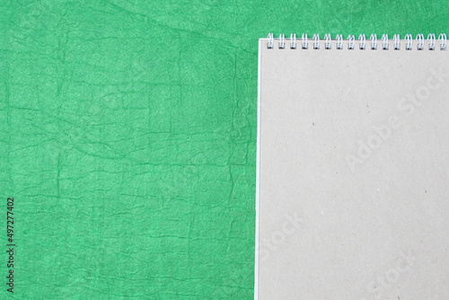 White and gray notepad sheet with spiral against the background of green fabric. Concept of analysis, study, attentive work. Stock photo with empty place for your text and design.