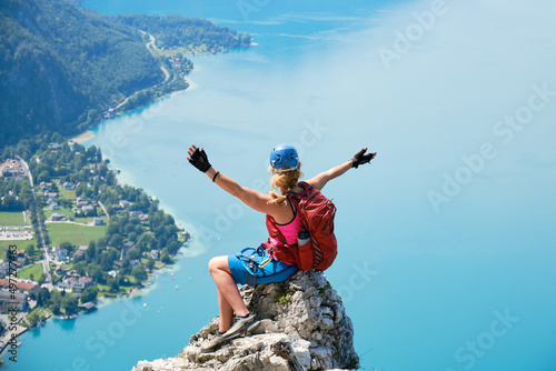 Via ferrata woman climber sits on top of a rock at Attersee, Austria, and spreads her arms. Happiness, courage, adventure, active, lake, summer.