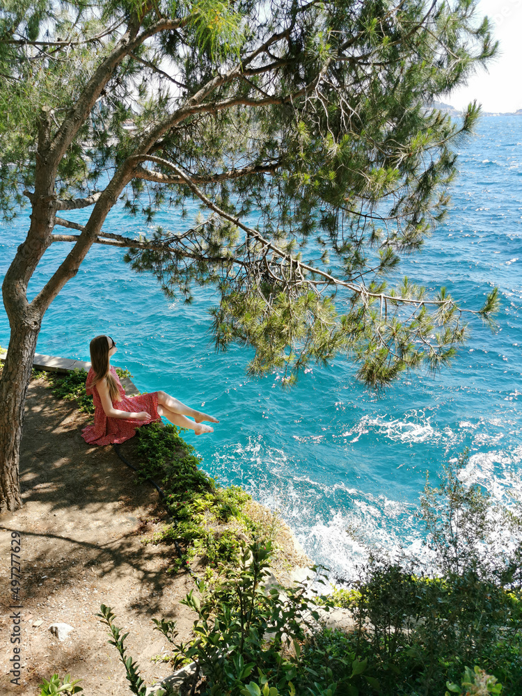 Obraz premium Girl tourist sits in a pine forest on the rocks on a background of beautiful seascape. Mediterranean Sea in Turkey, Kusadasi. Summer background.