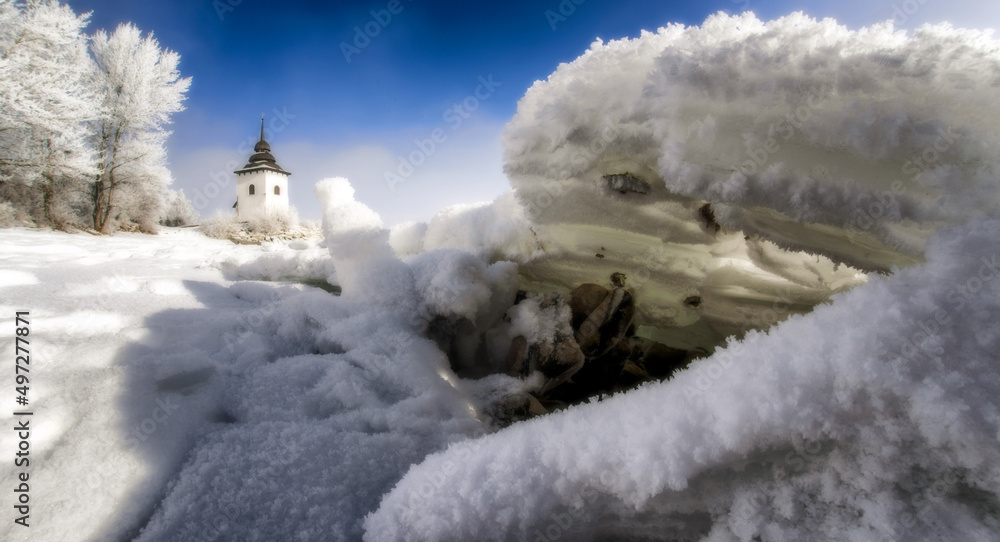 Frozen lake on cold winter morning. Ice floe on coastline. Tower of church at background Frozen lake on cold winter morning. Ice floe on coastline. Tower of church at background