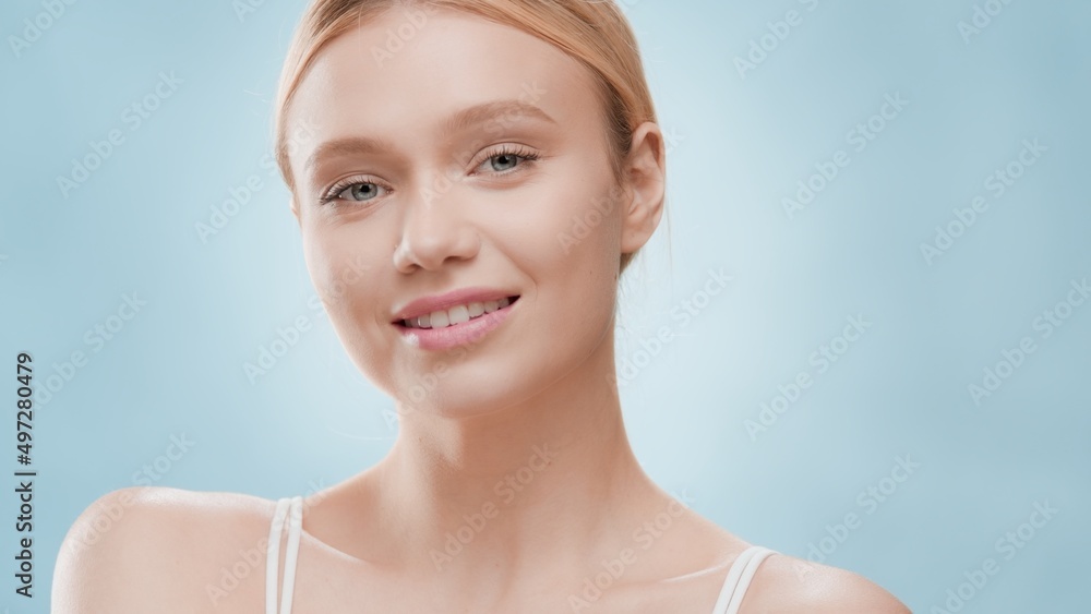 Beauty portrait of young blonde Caucasian woman who looks at camera and smiles on blue background | Skincare commercial concept Beauty portrait of young blonde Caucasian woman who looks at camera and smiles on blue background | Skincare commercial concept