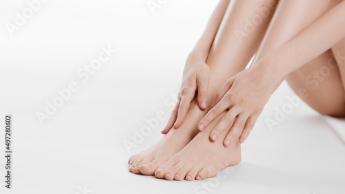 Fototapeta Naklejka Na Ścianę i Meble -  Close-up shot of white-skinned woman touches her smooth legs sitting on the floor on white background | Unwanted hair removal concept