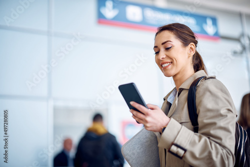Happy businesswoman checking schedule of her transportation on smart phone at departure area. © Drazen