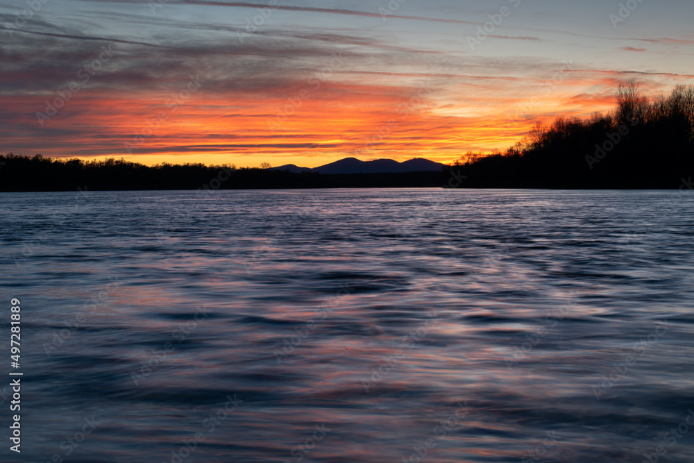 Mountain silhouette and colorful clouds reflecting in wavy water at dusk Mountain silhouette and colorful clouds reflecting in wavy water at dusk