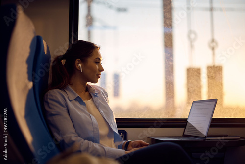 Young woman reads an email on laptop while commuting to work by train.