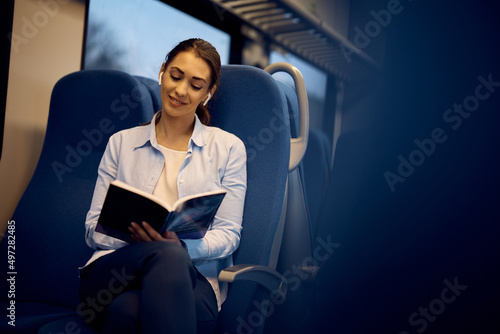 Young smiling woman travelling by train and reading book during the ride.