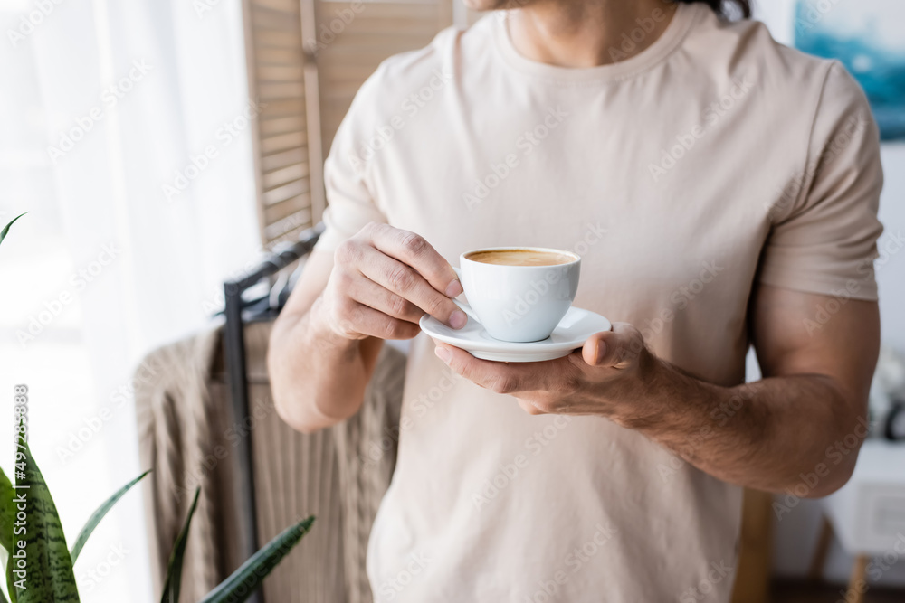 cropped view of man in t-shirt holding saucer with cup of coffee. cropped view of man in t-shirt holding saucer with cup of coffee.