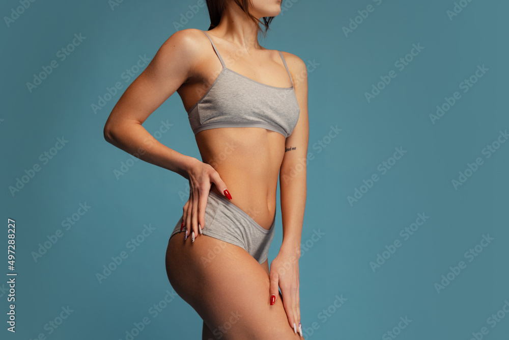 Cropped studio shot of slim, sportive female body in gray cotton underwear posing isolated over blue background. Fitness concept Cropped studio shot of slim, sportive female body in gray cotton underwear posing isolated over blue background. Fitness concept