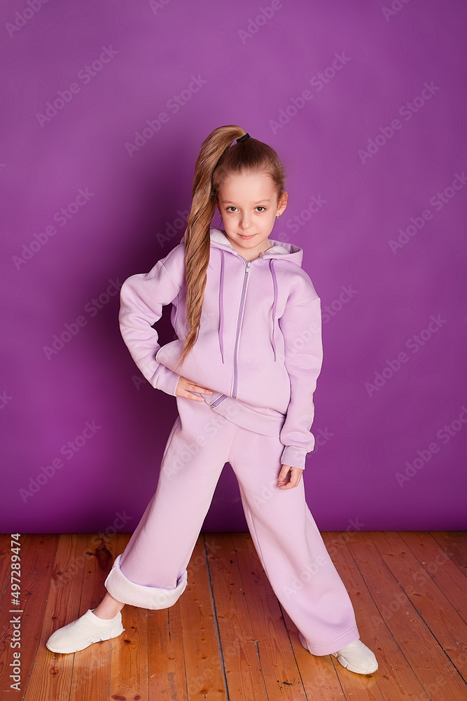 a smiling little girl in a soft purple suit on a purple background in the studio. The concept of treats for children's birthday