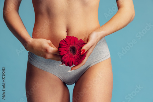 Cropped image of sportive female body, belly with red gerbera flower isolated over blue studio background photo