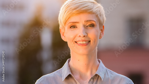Portrait outdoors female happy smiling face natural makeup caucasian head with short hair mature 40s business woman standing posing outdoor in sunlight sunset sunbeams looking at camera with smile