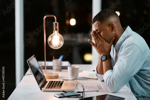 Running a business is so much stress. Shot of a handsome young businessman feeling stressed out while working late in his office. photo