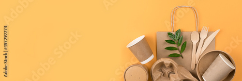 Banner with eco-friendly tableware - kraft paper food utensils, paper containers and cups, drinking straws and wooden cutlery on orange background with copy space. Sustainable food paper packaging