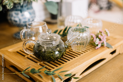 Delicious freshly brewed green tea ceremony. Glass tea cups with transparent glass tea pot standing on the wooden tray  decorated with small flowers 