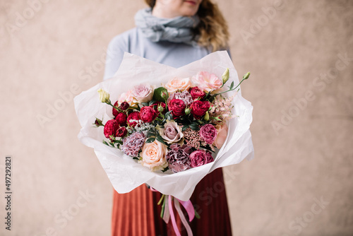 Very nice young woman holding big and beautiful bouquet of fresh roses, carnations, eustoma in pink and burgundy colors, cropped photo, bouquet close up