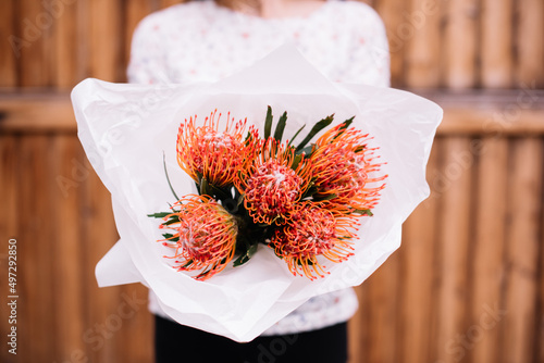 Very nice young woman holding exotic and beautiful mono bouquet of fresh orange nutan proteas , cropped photo, bouquet close up on the wooden background photo