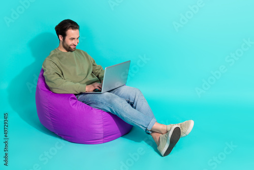 Full length profile side photo of young guy sit violet armchair use laptop chat report isolated over turquoise color background