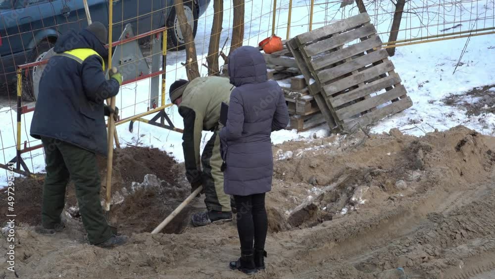 Two builders dig a hole with shovels in the frozen solid ground in winter. Digging trenches for laying pipelines and sewers. A construction crew is working on the construction site. Two builders dig a hole with shovels in the frozen solid ground in winter. Digging trenches for laying pipelines and sewers. A construction crew is working on the construction site.