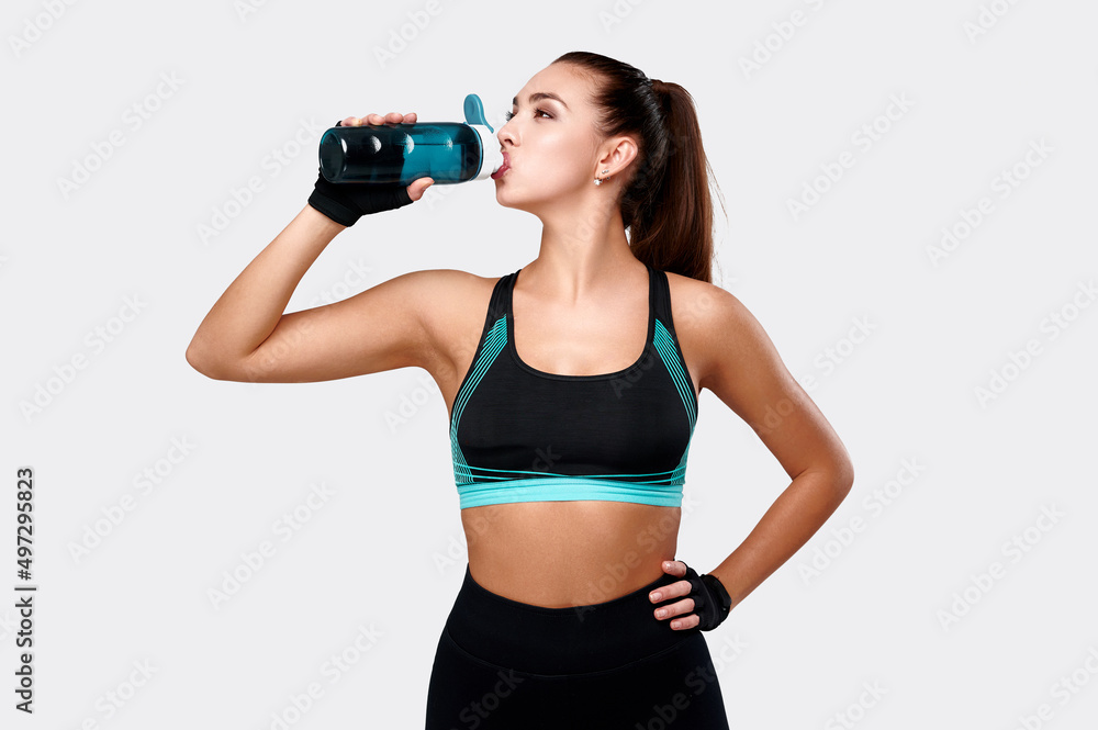 White fitness model wearing sport clothes drink water on gray isolated background. Healthy lifestyle and beauty White fitness model wearing sport clothes drink water on gray isolated background. Healthy lifestyle and beauty