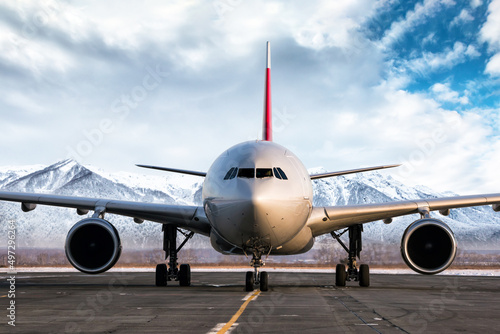 Front view of a wide body passenger aircraft at the airport apron on the background of high picturesque mountains