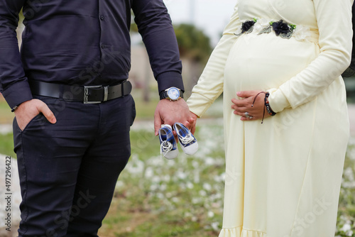 View of a pregnant woman with shoes in their hands standing in an outdoor shoot with her partner