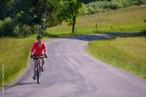Smiling, active, mature woman wearing bike helmet and sunglasses biking on a country road on a spring summer day.