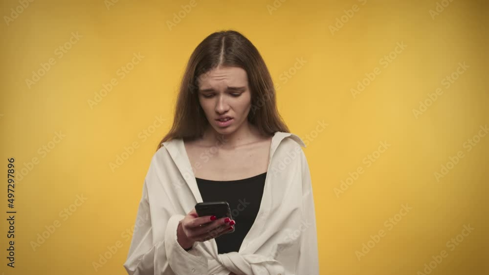Young adult caucasian woman is upset by the news on her smartphone on a bright yellow background