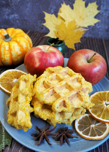 Belgian gluten-free pumpkin waffles lie on a brown plate with a dry slice of lemon and stars of anise, pumpkin, apples on a background of yellow maple leaves on the table