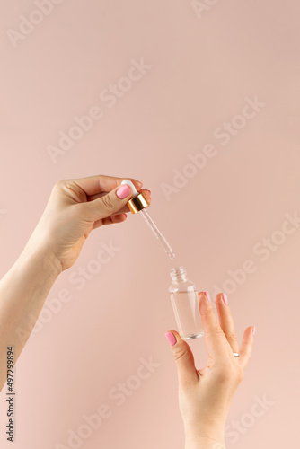 Female hands drip oil with a pipette inside a dropper with a care product on a light pink background. Care cosmetics.