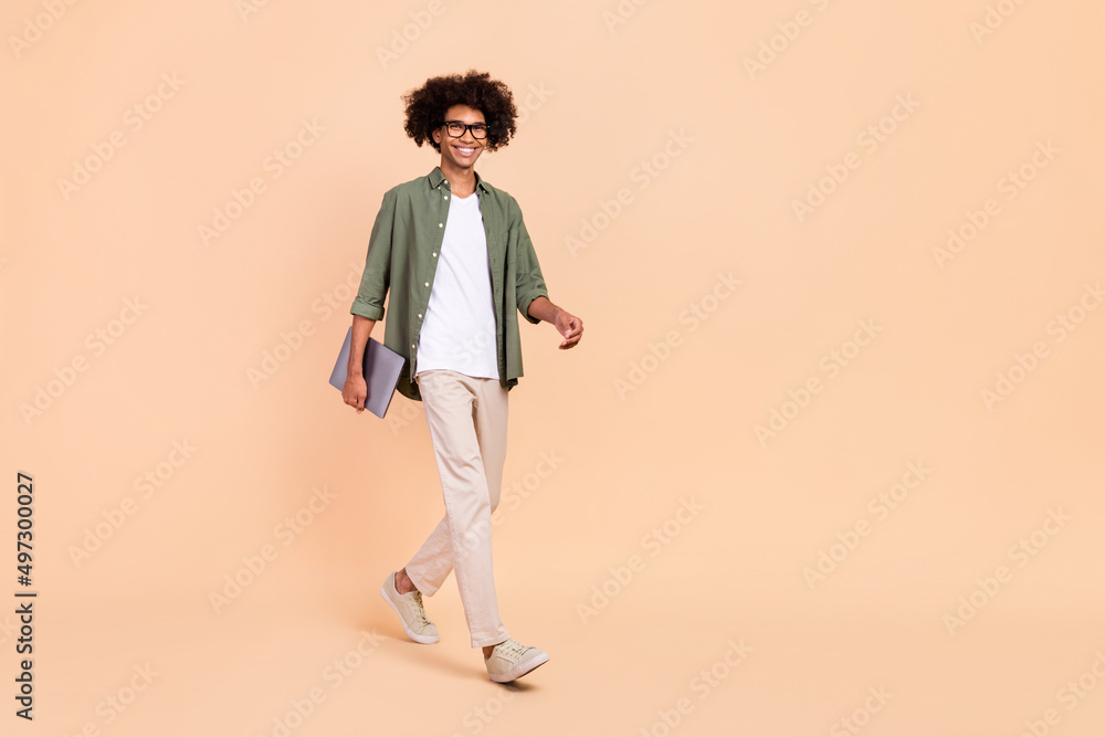 Full length body size view of attractive cheerful skilled guy going holding laptop startup project isolated over beige pastel color background Full length body size view of attractive cheerful skilled guy going holding laptop startup project isolated over beige pastel color background