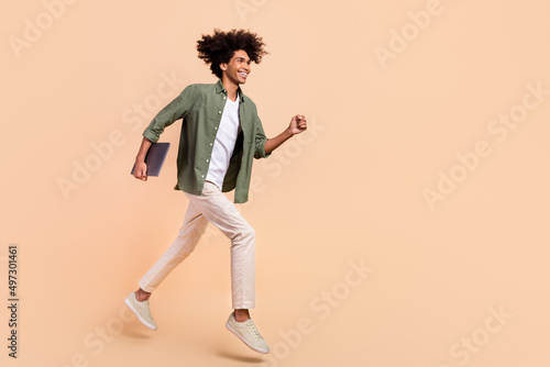 Full length body size view of attractive cheery trendy guy jumping holding laptop running success isolated on beige pastel color background