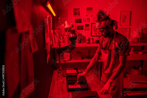 Photography Creative young indian man wearing apron and protective gloves developing photos