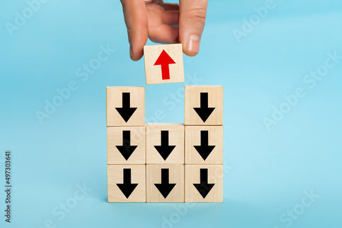 Businessman hand picked wooden block with red arrow facing the opposite direction black arrows, unique, think different, individual and standing out from the crowd concept, technology innovation