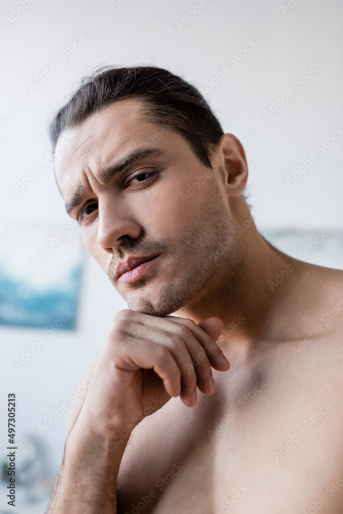serious and shirtless man looking at camera at home.
