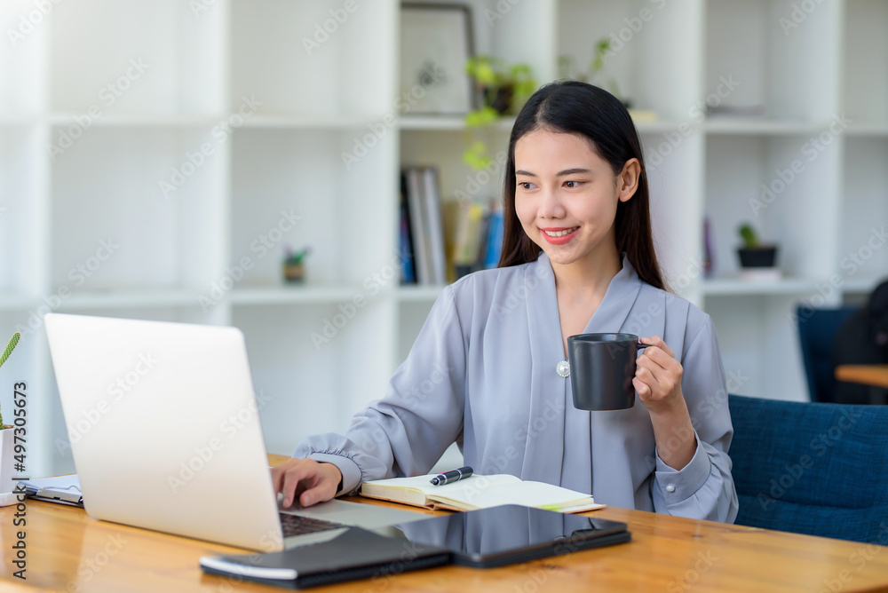 Happy beautiful Asian business woman holding a coffee mug and laptop at the office. Happy beautiful Asian business woman holding a coffee mug and laptop at the office.